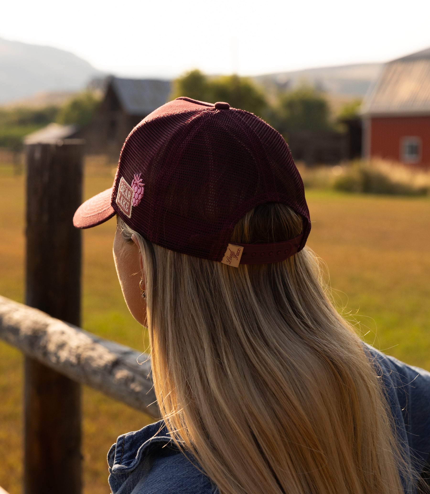 Woman leaning on a fence rail in a Raspberry Days cap