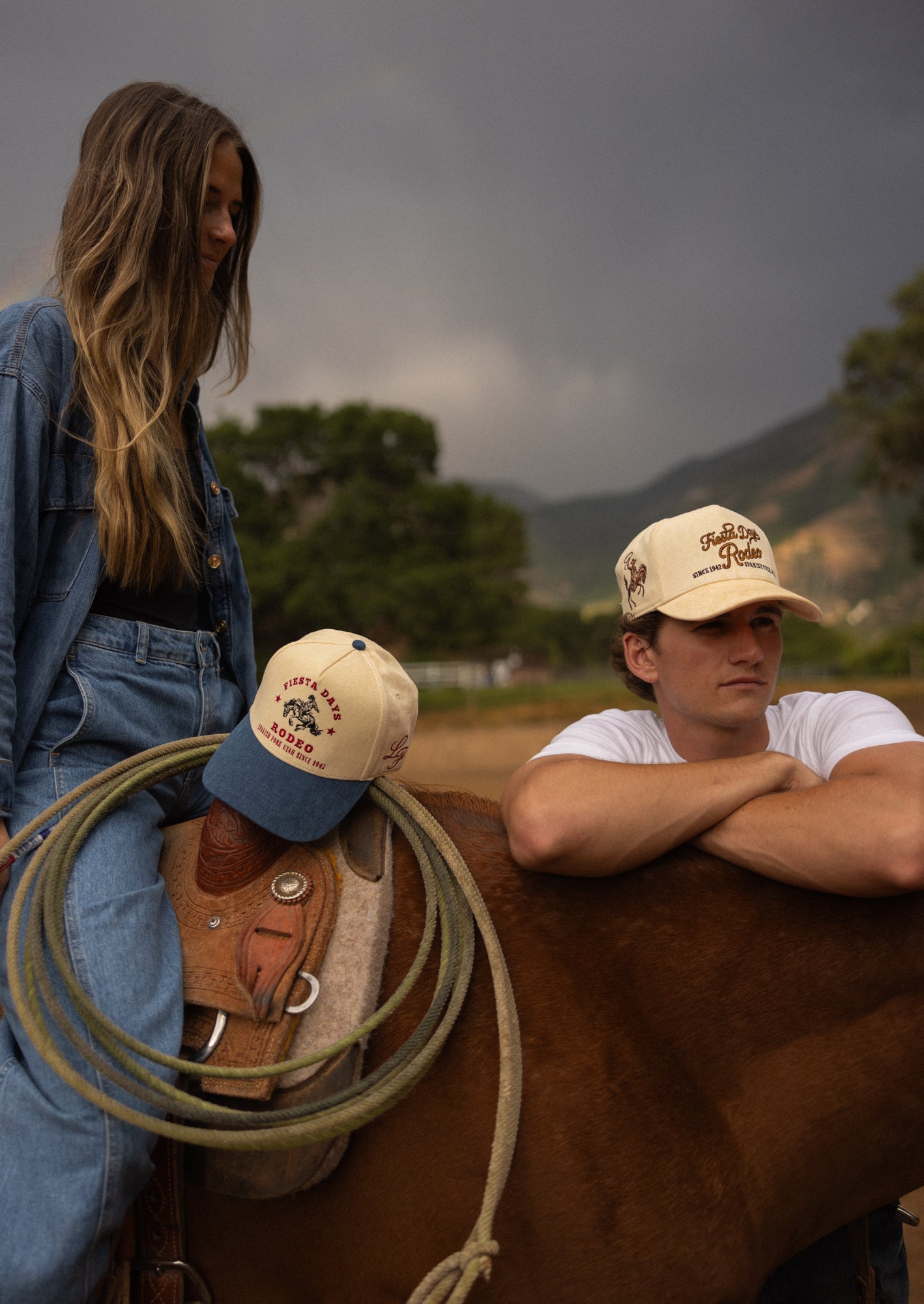 Two riders on horseback in Loud Face caps at golden hour