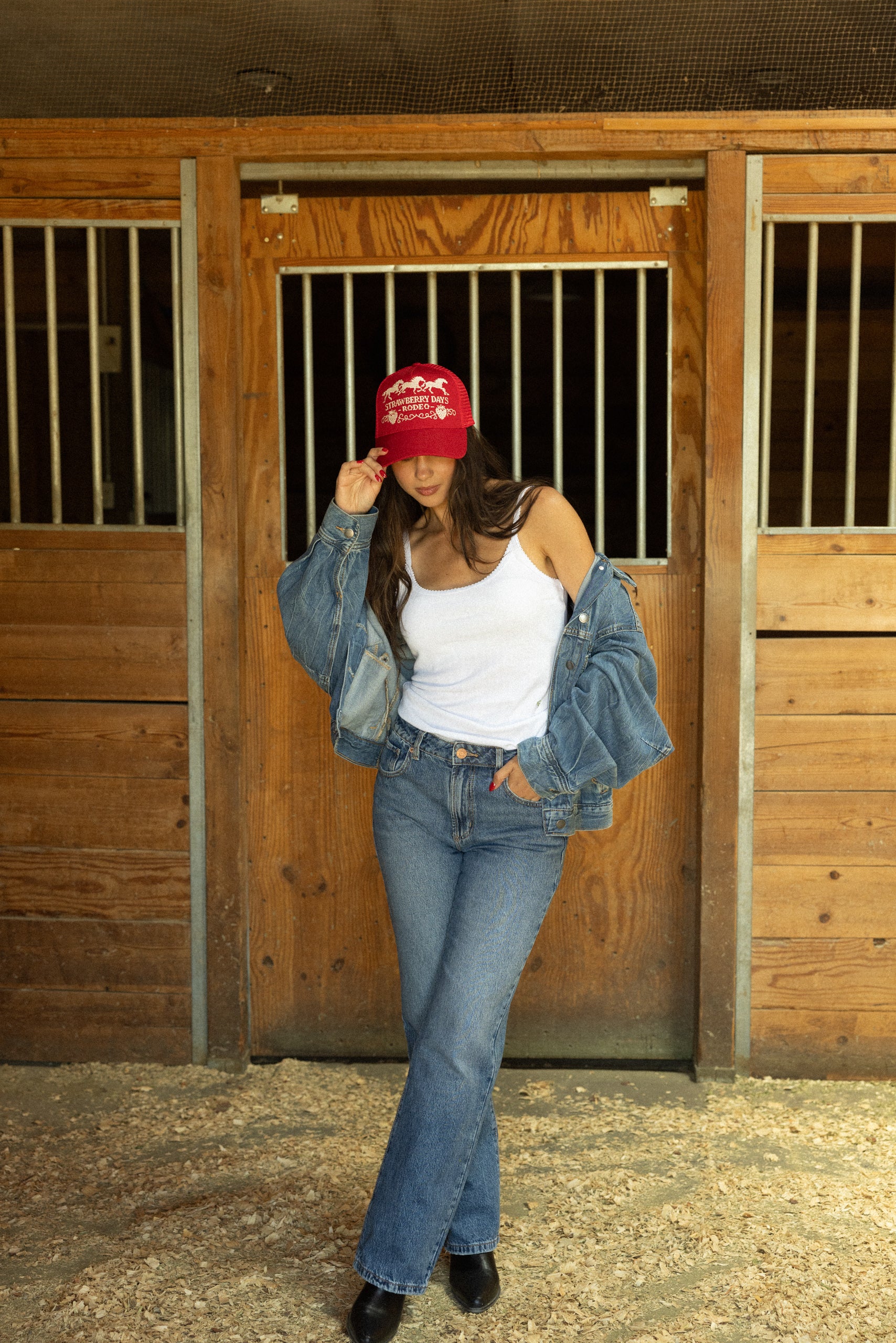Woman in a barn doorway wearing a red Strawberry Days Rodeo trucker hat