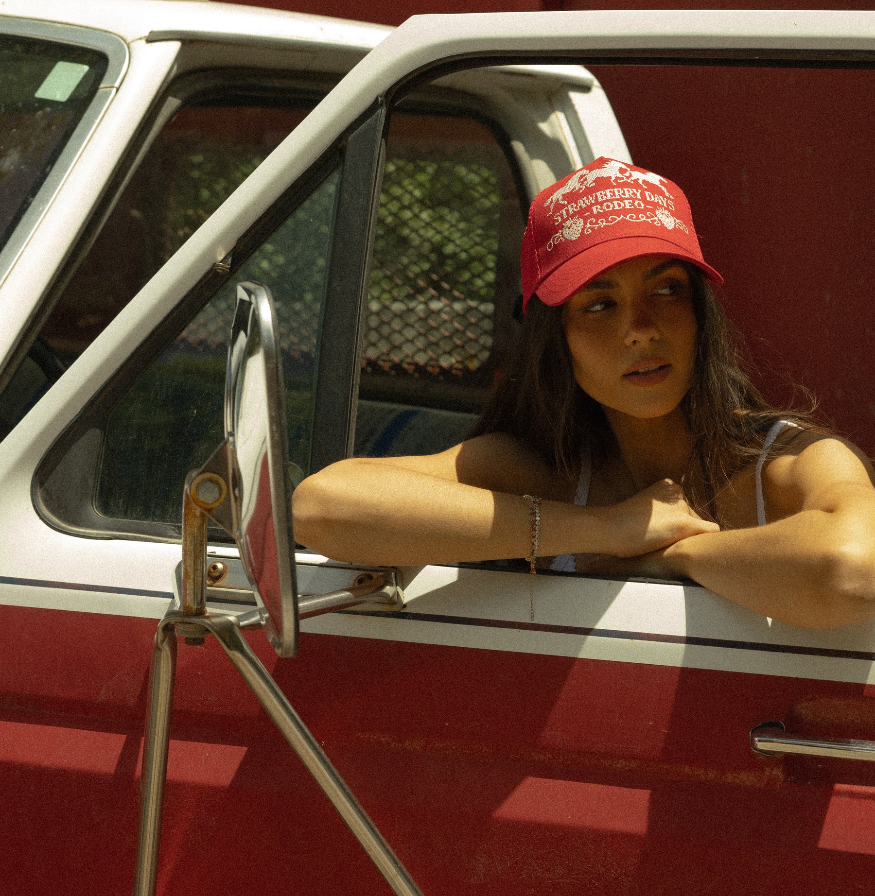 Woman leaning out of a red truck window in a Loud Face rodeo hat