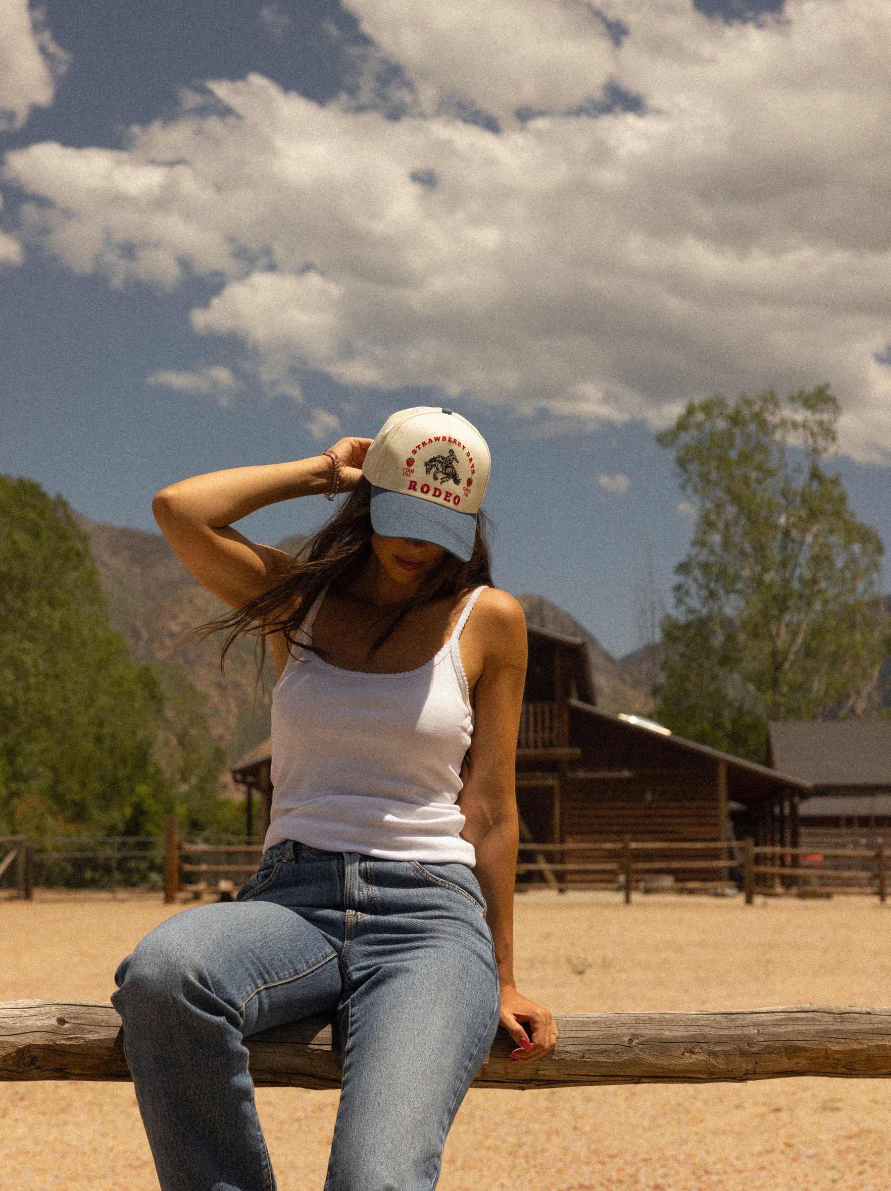 Woman seated outside a barn wearing a Loud Face trucker hat